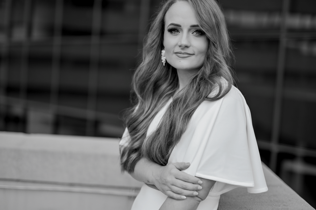 Convert this portrait photo to black and white. Keep everything exactly the same — the composition, the woman, the pose, the background — just remove all colour so it becomes a crisp, elegant monochrome image.